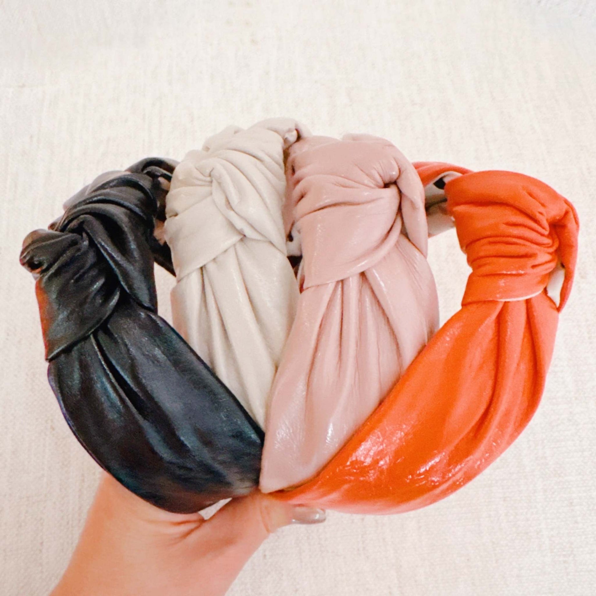 Patent leather Hampton lady headband in black, beige, pink, and orange colors with a knotted design and medium hair-holding capacity