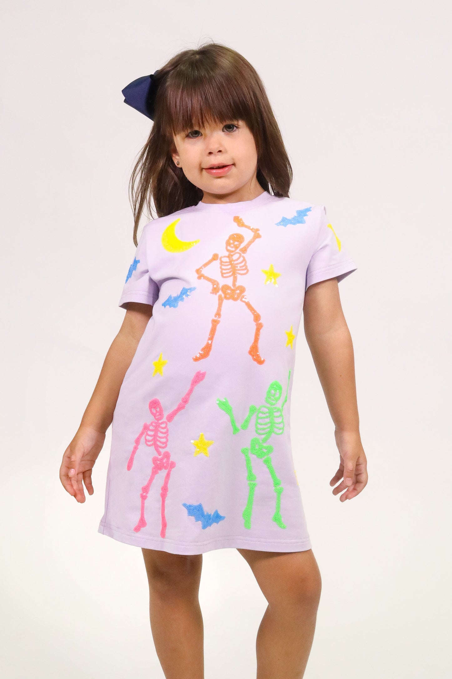 Girl wearing lavender skeleton dress with colorful skeletons and Halloween motifs