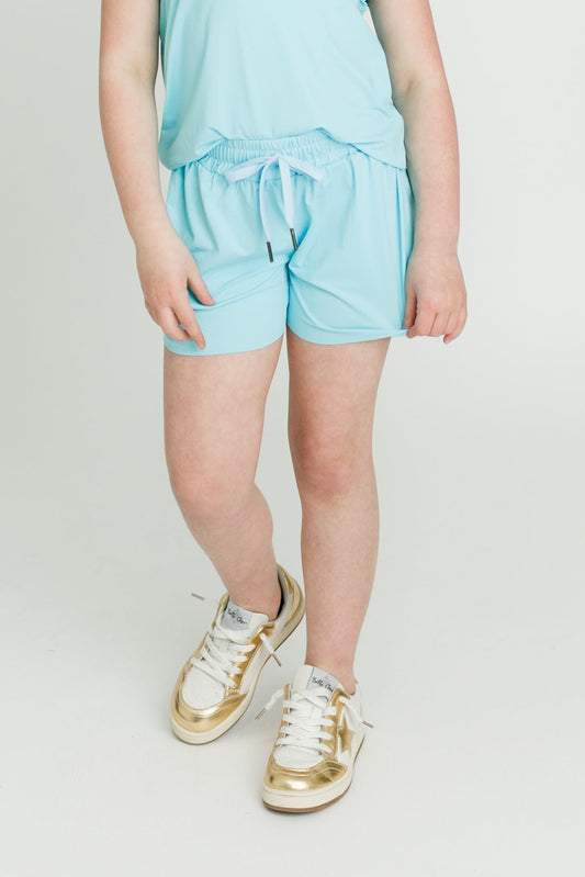 Child wearing light blue kid butterfly shorts with gold and white sneakers.