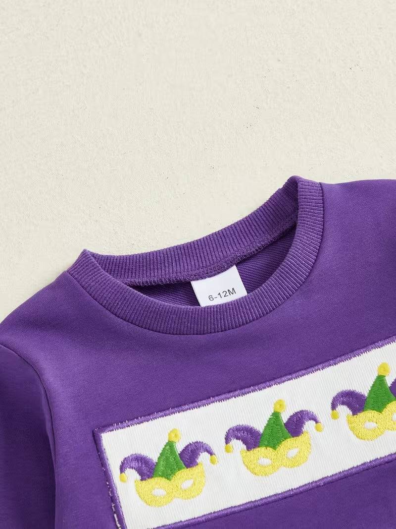 Purple sweatshirt with Mardi Gras-themed design on a beige background