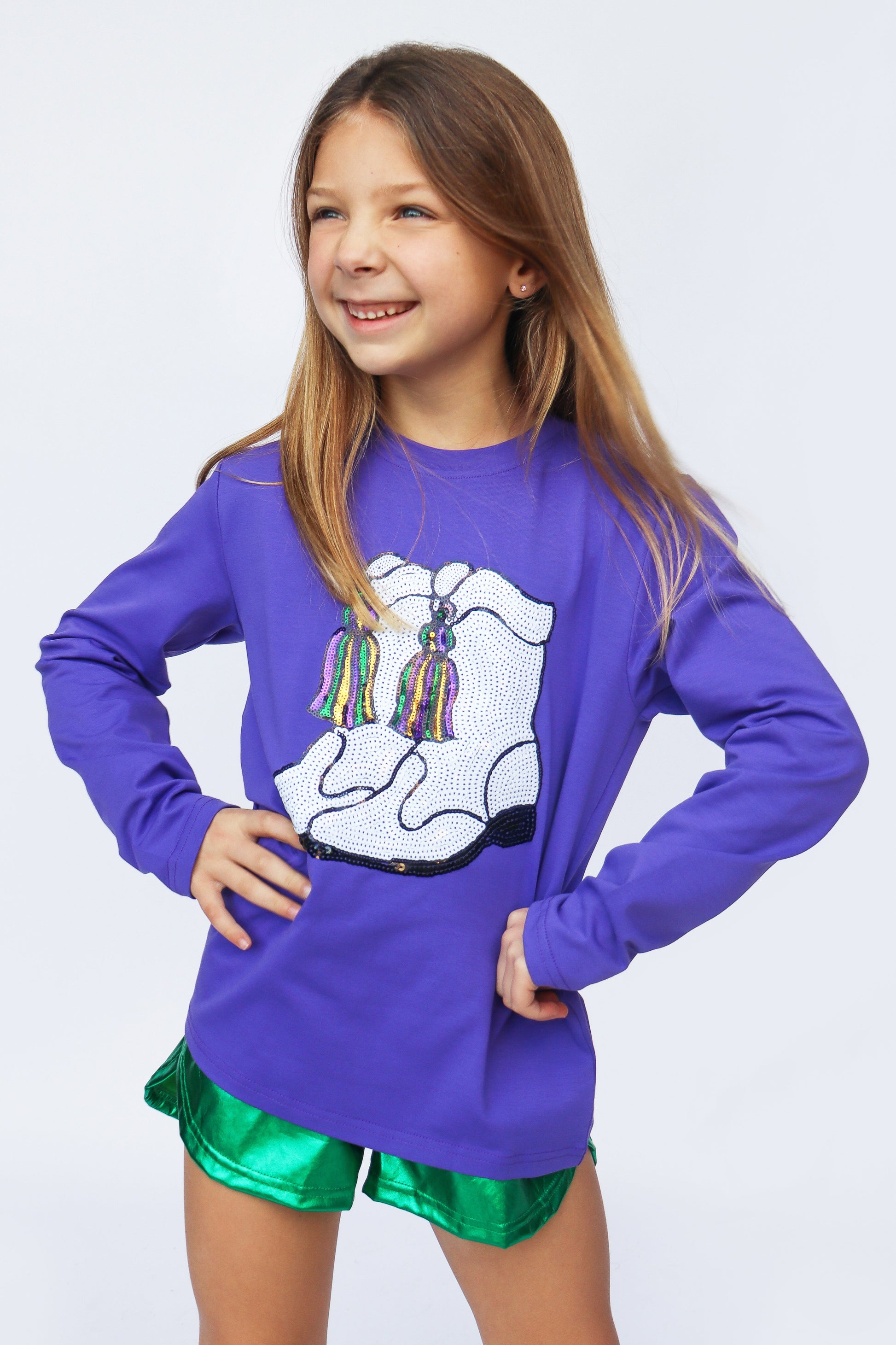 Young girl wearing a purple shirt with a white graphic design and green shorts on a light gray background