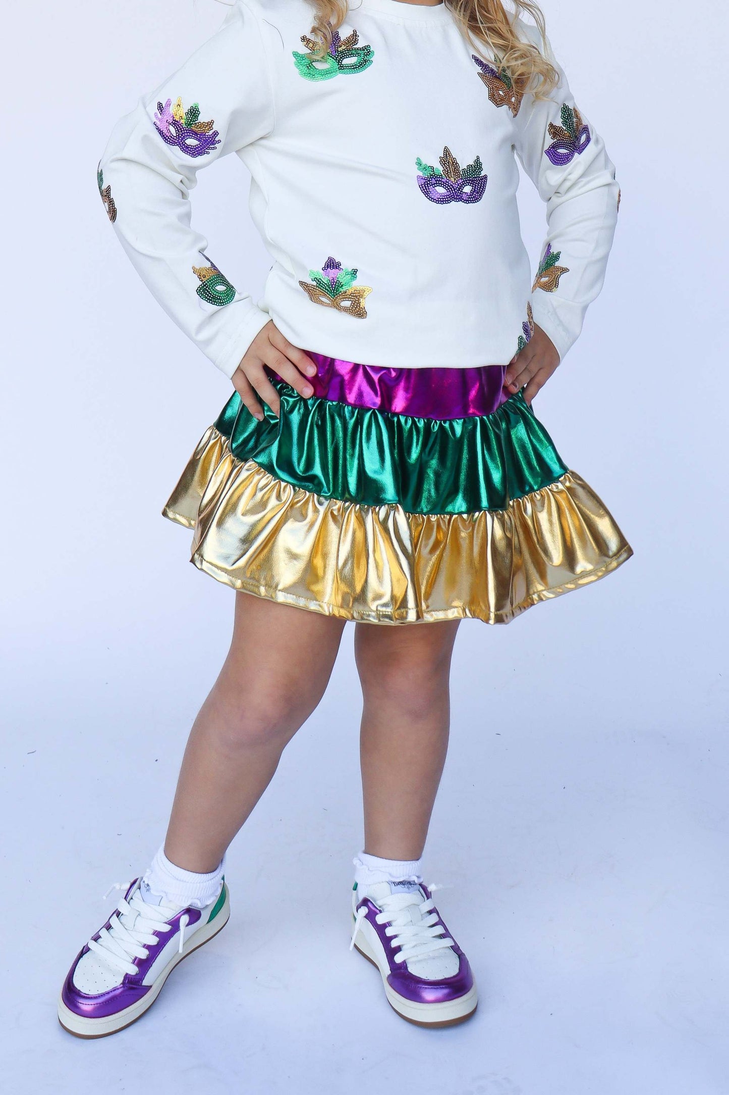 Child wearing a colorful outfit with a white sweater, multicolored skirt, and sneakers on a light gray background