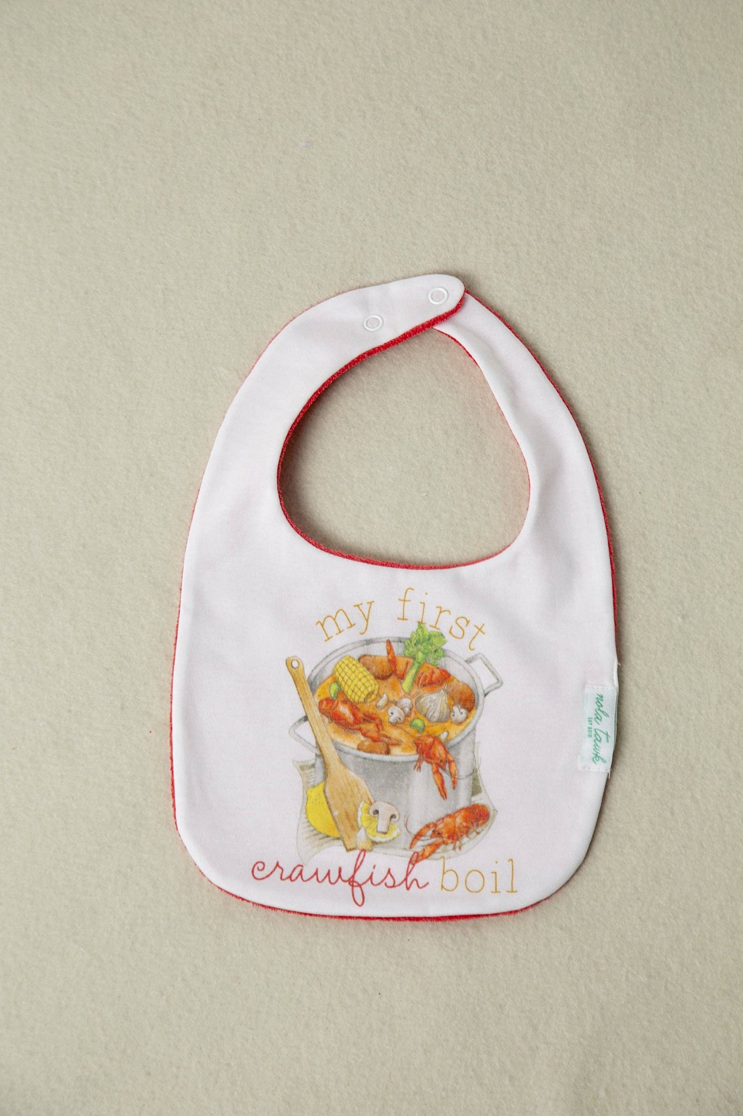 Baby bib with 'my first crawfish boil' text and graphics on a beige background