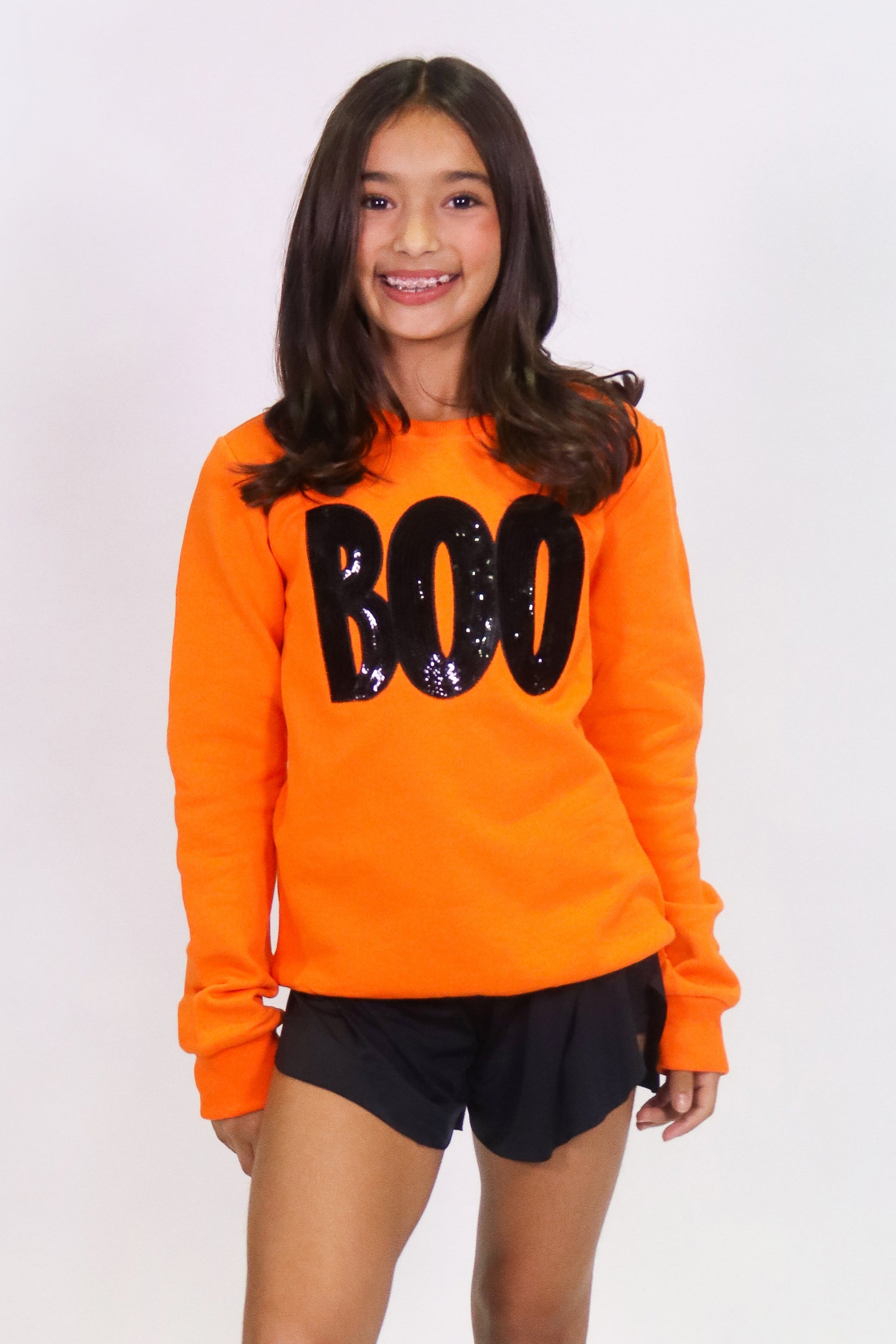 Girl wearing orange Boo sweatshirt with black sequin letters and black shorts