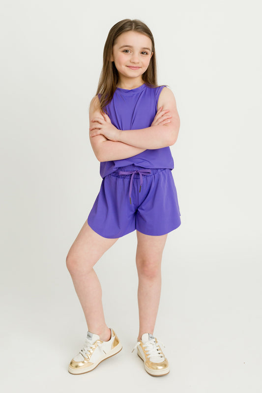 Girl wearing purple kid butterfly shorts and matching sleeveless top standing with arms crossed