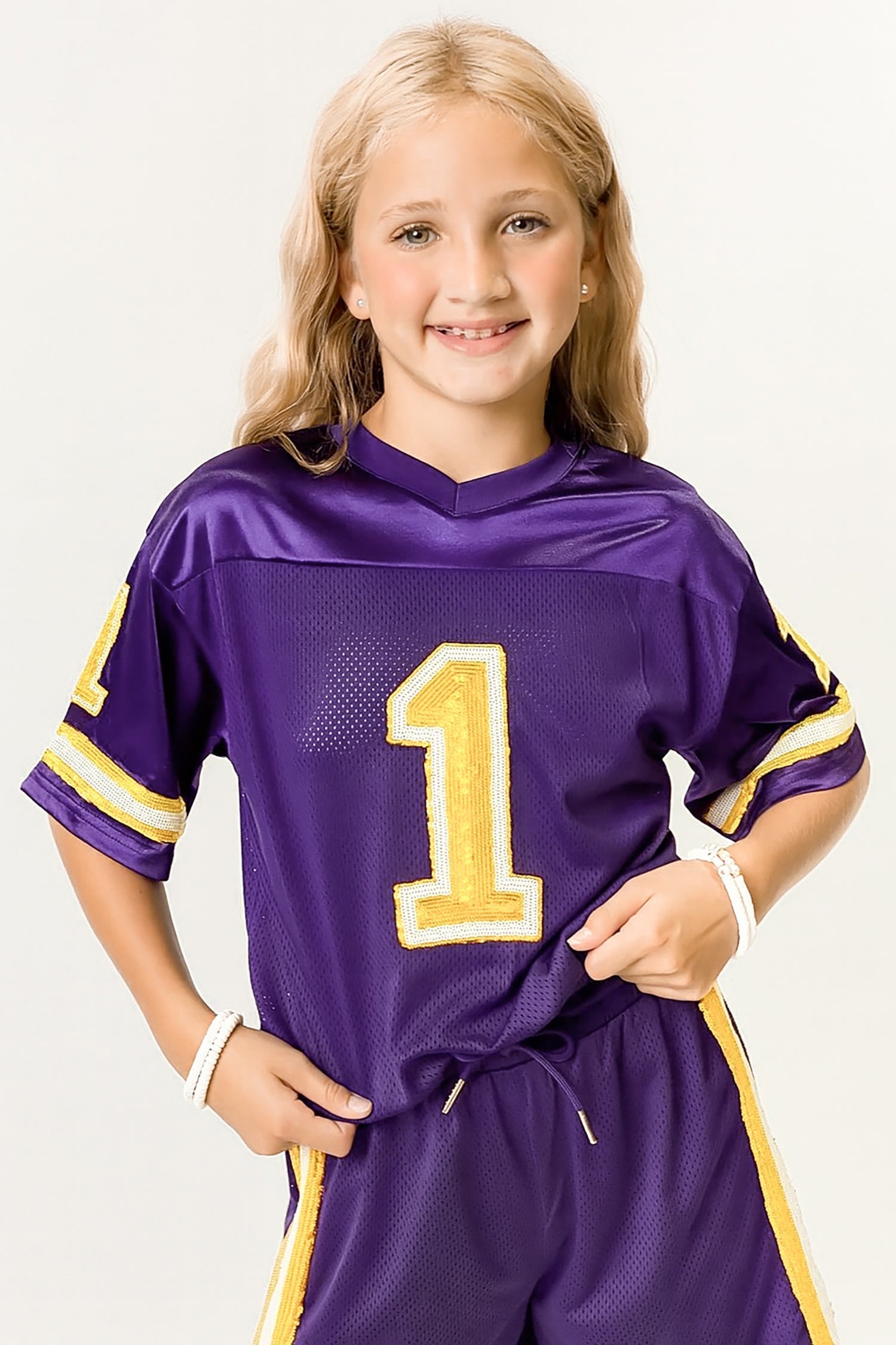 Child wearing purple and yellow sequin kid jersey with number 1 front and matching shorts