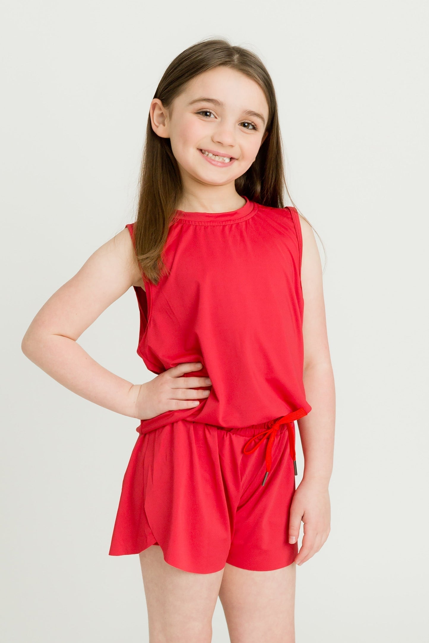 young girl wearing red high low kid tank and matching shorts smiling standing against white background