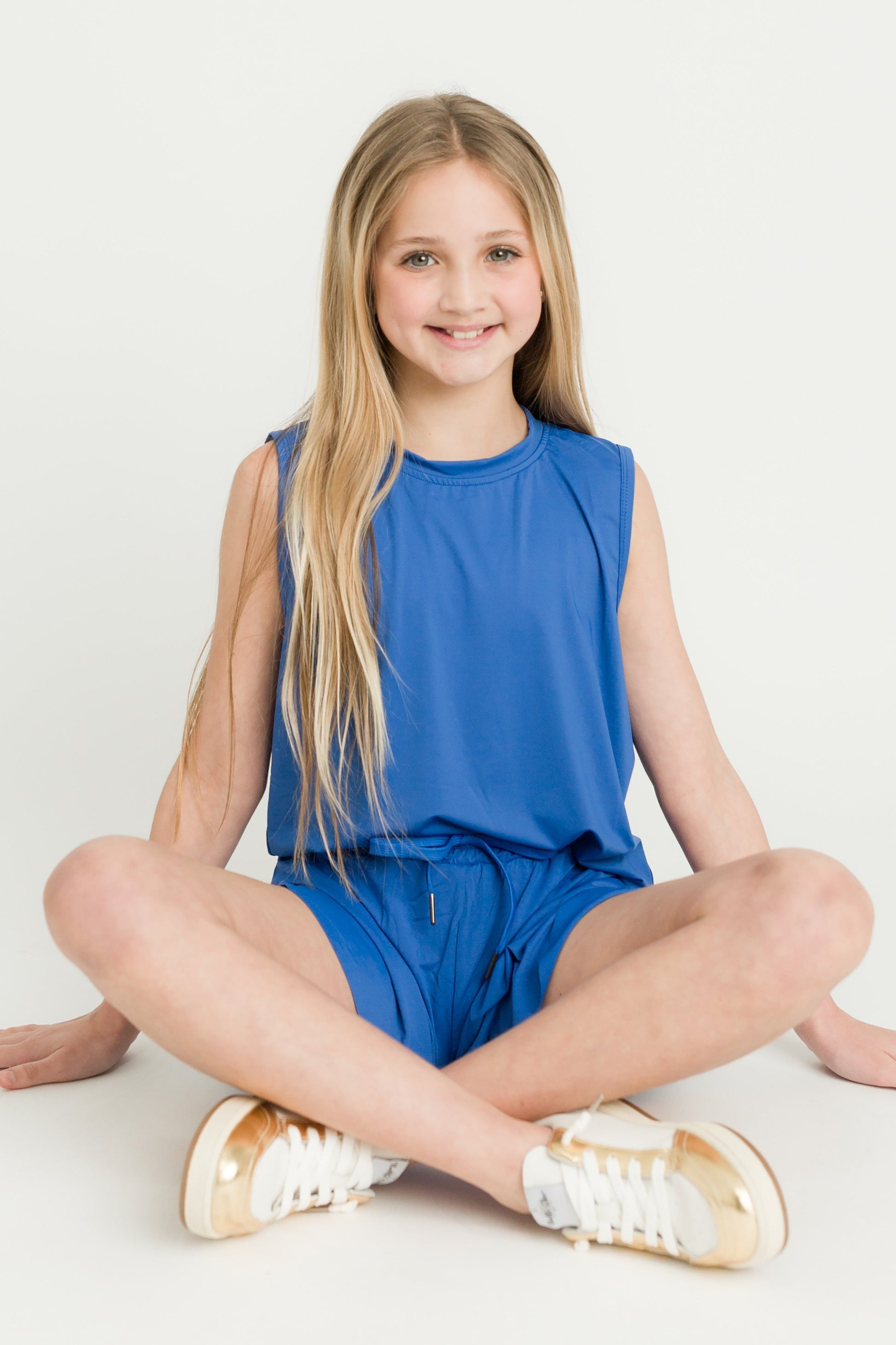 Girl wearing royal blue high low kid tank sitting cross-legged smiling