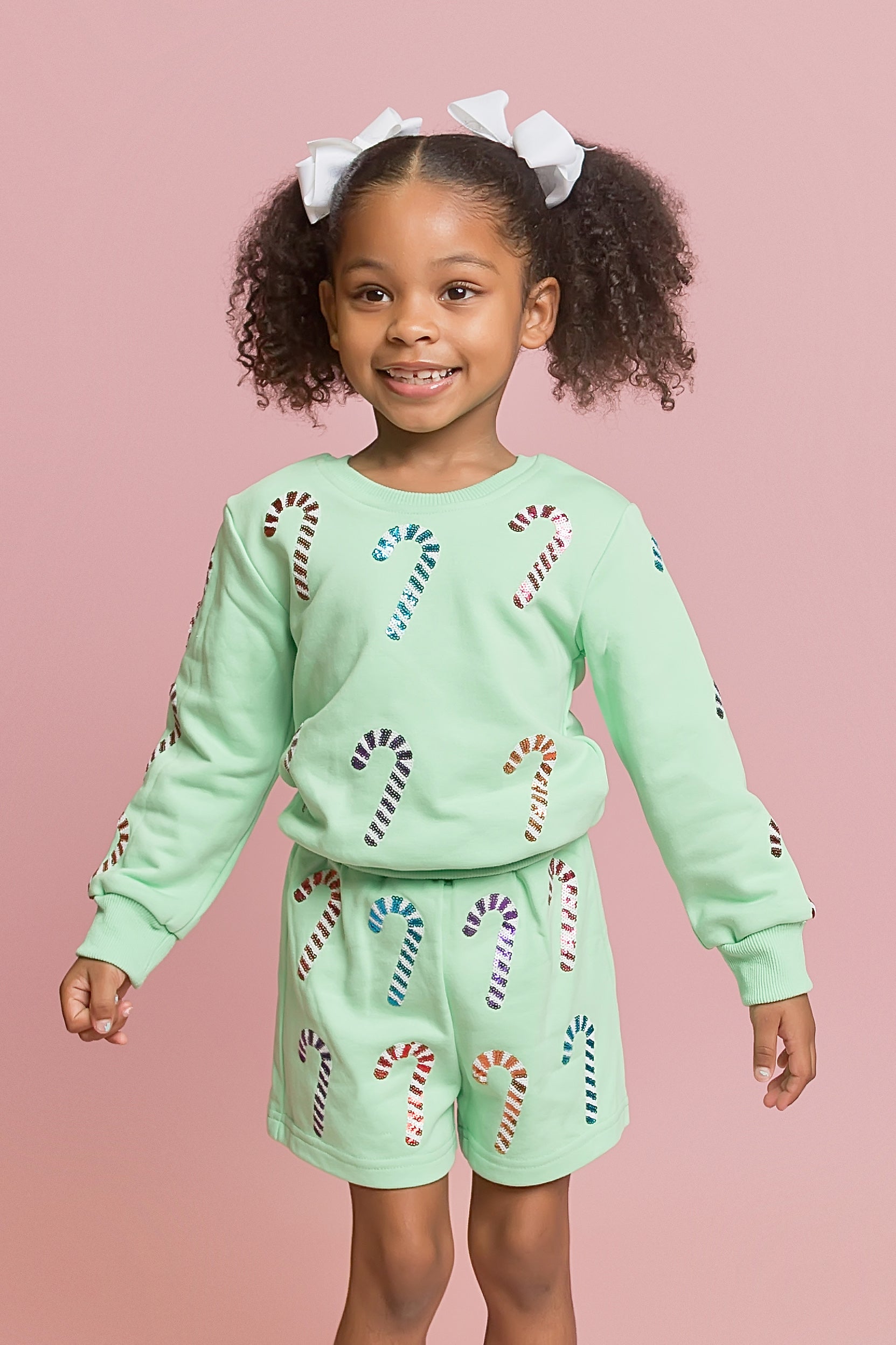 Child wearing a light green outfit with candy cane patterns on a pink background