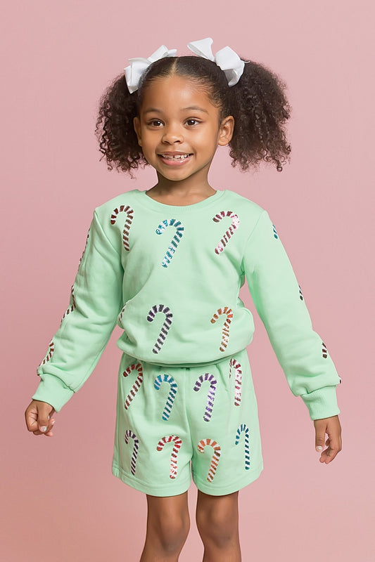 Child wearing a light green outfit with candy cane patterns on a pink background