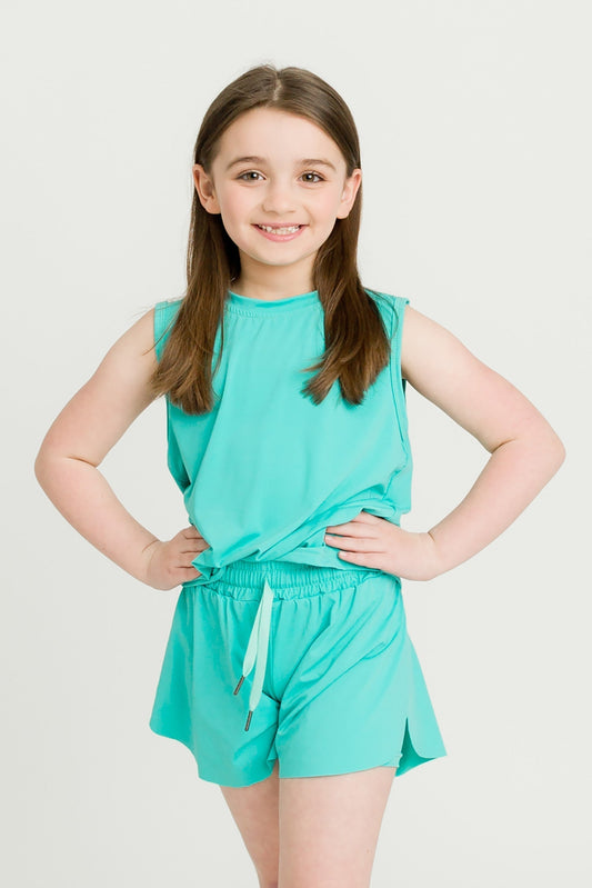 young girl wearing teal high low kid tank and matching shorts smiling