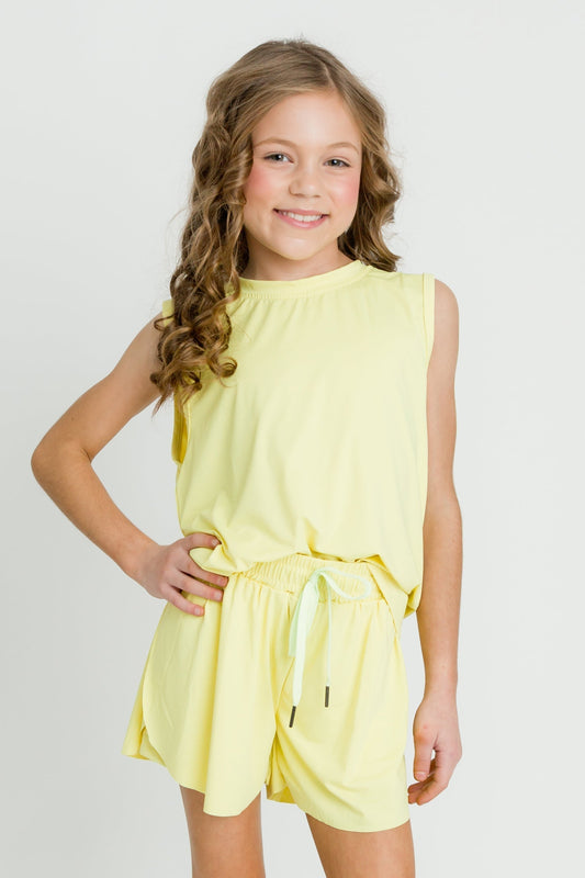 Smiling child wearing yellow high low kid tank with matching shorts against white background