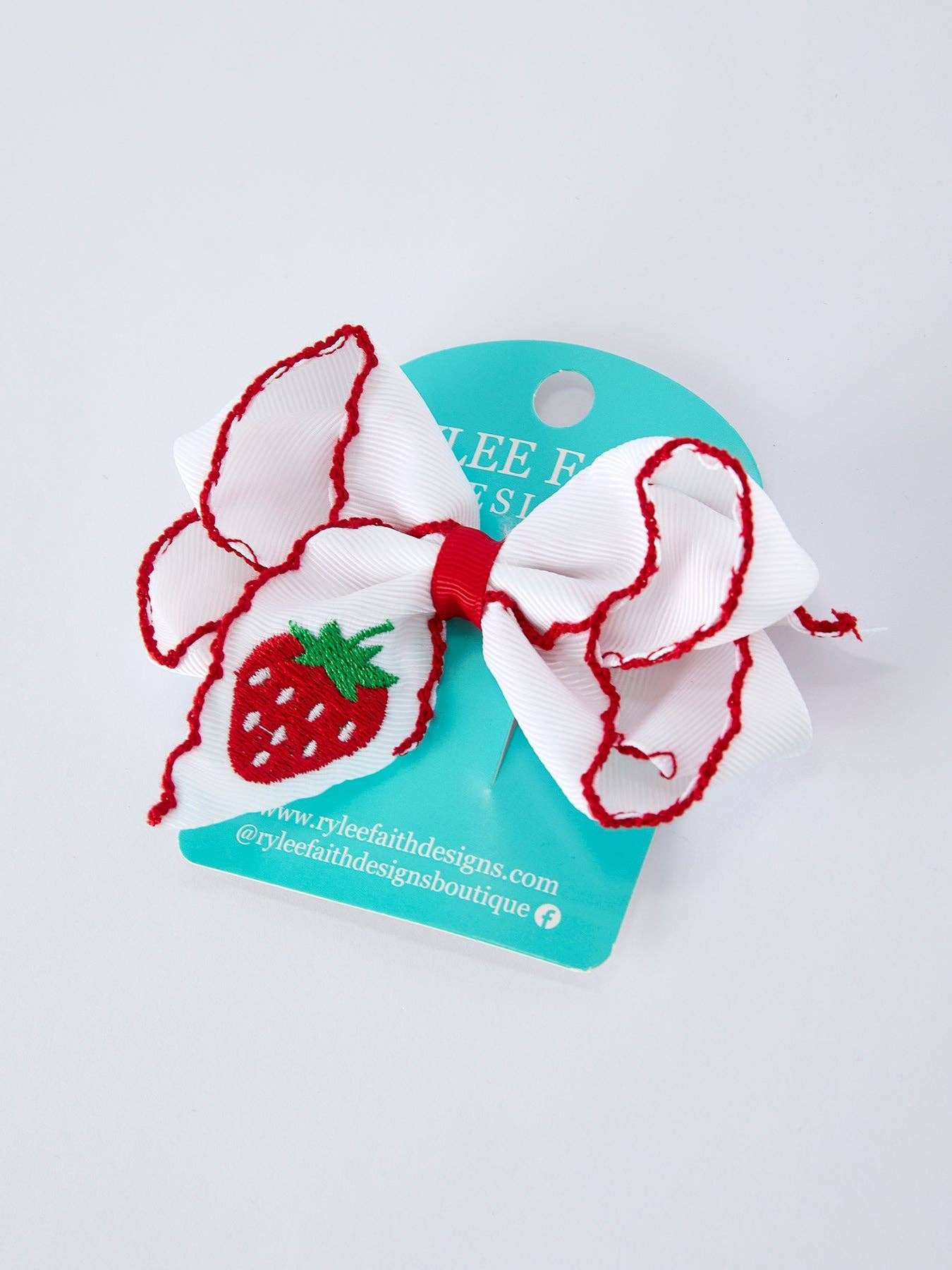 White bow hair clip with red accents on a blue card with brand name