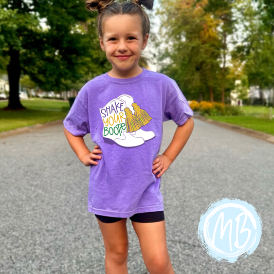 Bootie Mardi Toddler & Youth Tee with whimsical Mardi Gras boots design, worn by child outdoors.