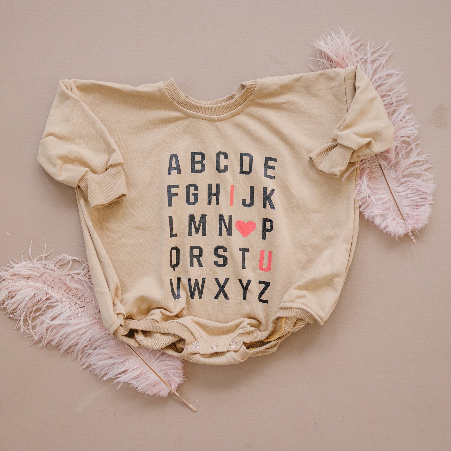 Beige baby onesie with alphabet print on a beige background