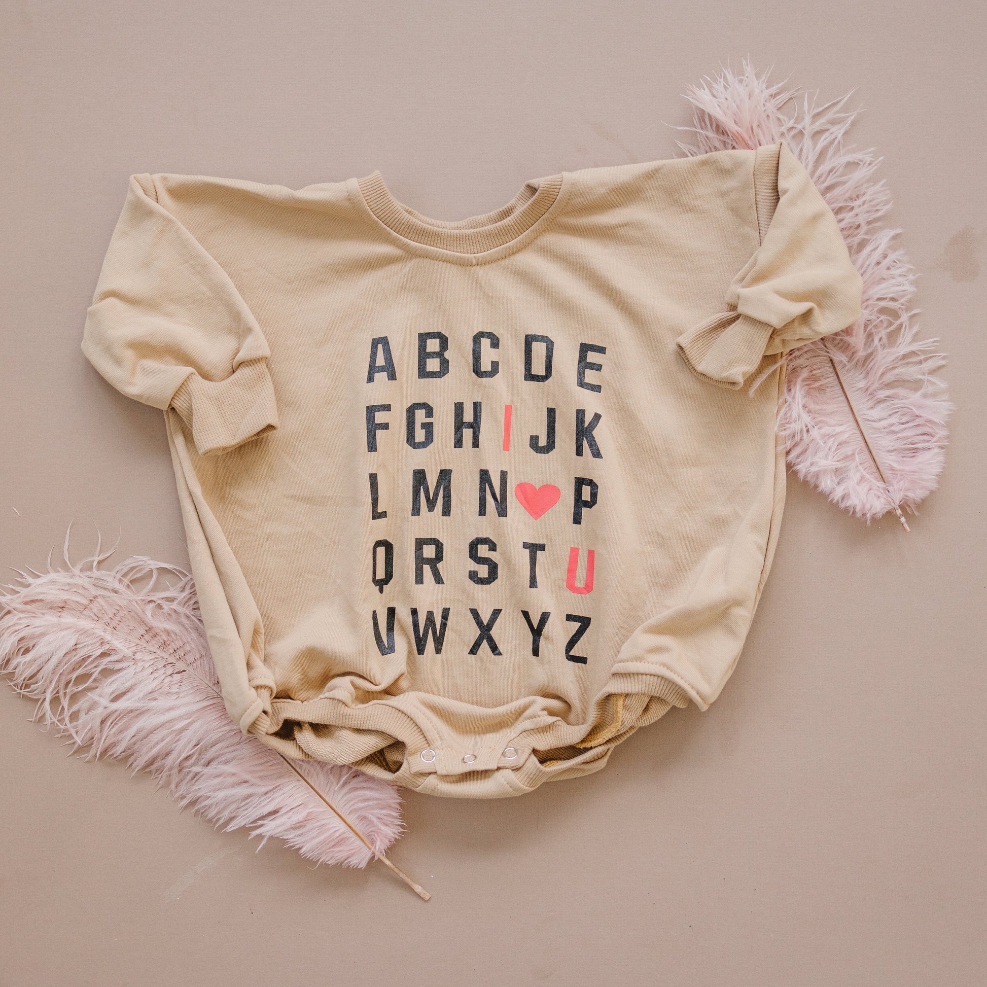 Beige baby onesie with alphabet print on a beige background