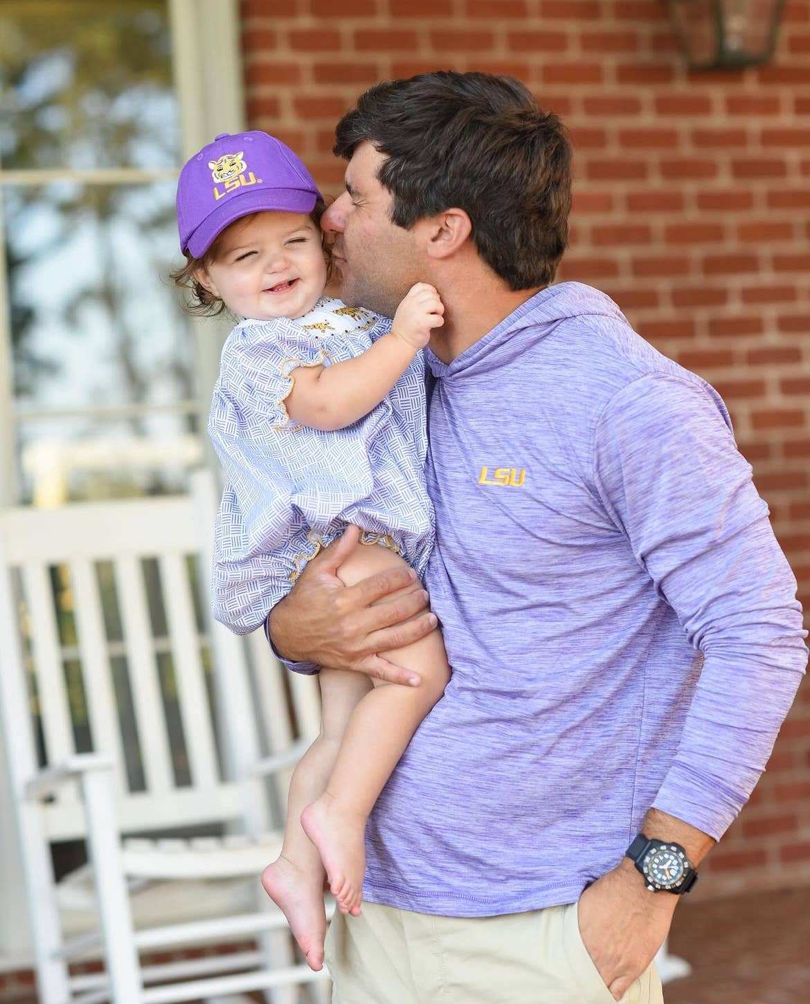 Little girl being held by dad wearing an lsu baseball cap